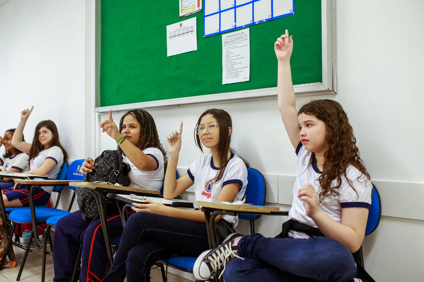 Estudantes em sala de aula levantam a mão para participar