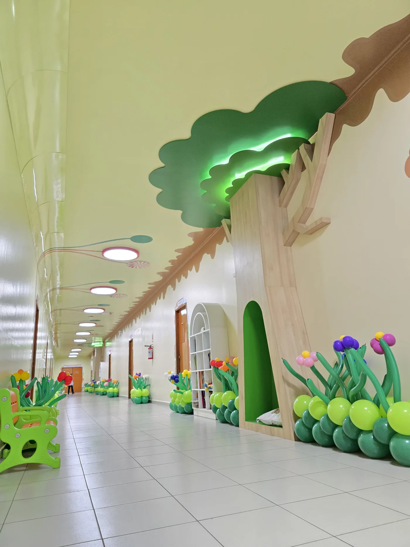 Corredor temático com árvore decorativa, estante de livros e iluminação colorida